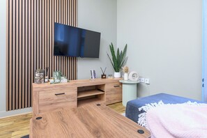 Un salon moderne avec un meuble TV en bois, un téléviseur à écran plat, une plante en pot et un canapé bleu.