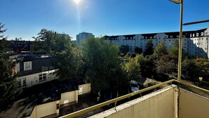 Uitzicht vanaf een balkon over een woongebied met een rij appartementen, een helderblauwe lucht en een stralende zon.