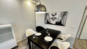 Een eethoek met een zwarte tafel, witte stoelen, een schilderij aan de muur en een vloerlamp.