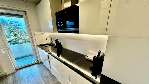 Een moderne keuken met een zwart aanrecht, witte kastjes en een ingebouwde oven.
