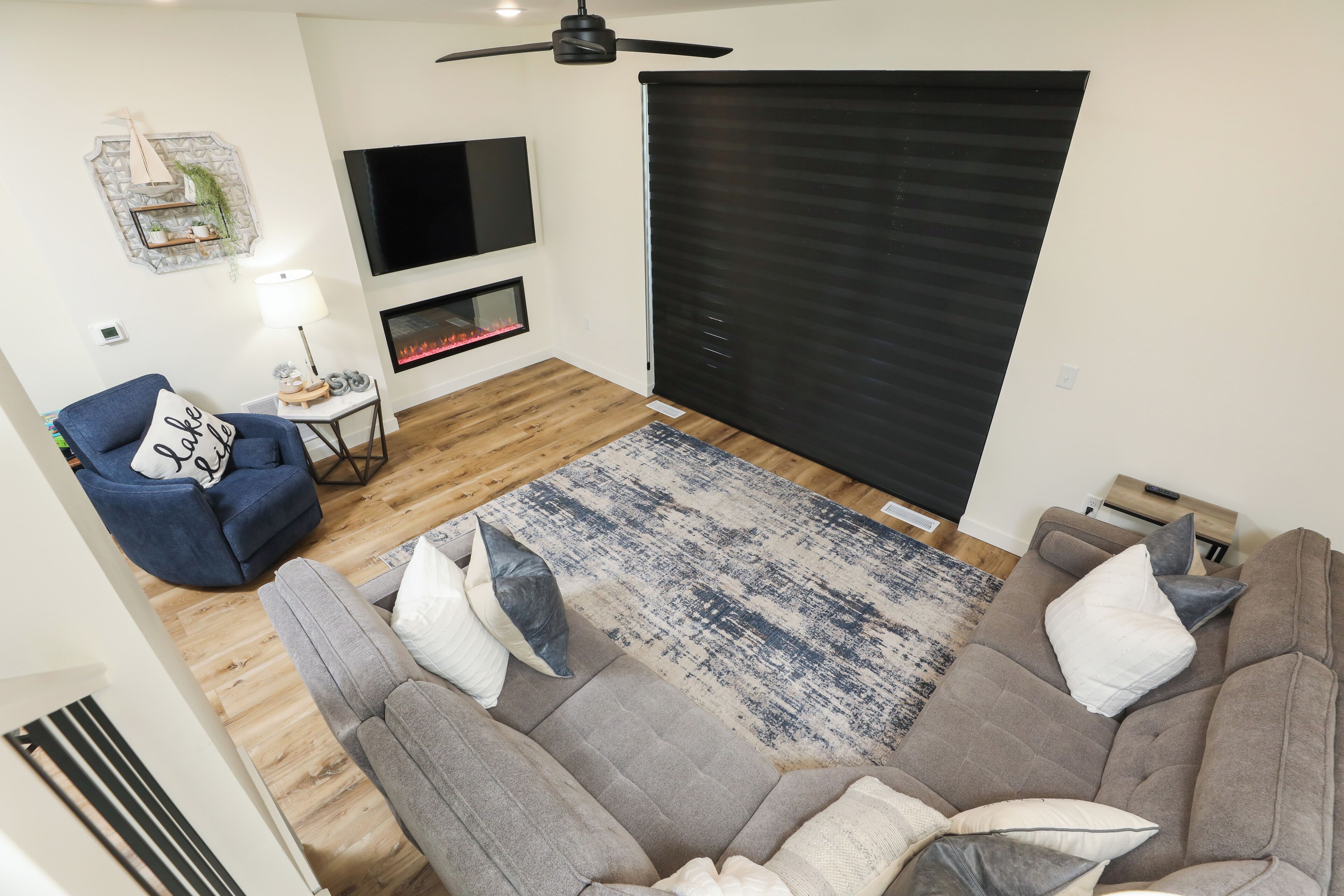 Uma sala de estar com sofá, poltrona, televisão, lareira e ventilador de teto.