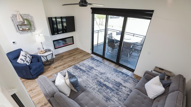 Ein Wohnzimmer mit grauem Sofa, blauem Sessel, Fernseher, Kamin und einer großen Glasschiebetür, die auf eine Außenpatio führt.