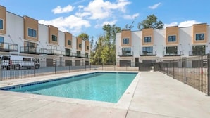Ein modernes Apartmenthaus mit Pool, umzäuntem Parkplatz und blauem Himmel.