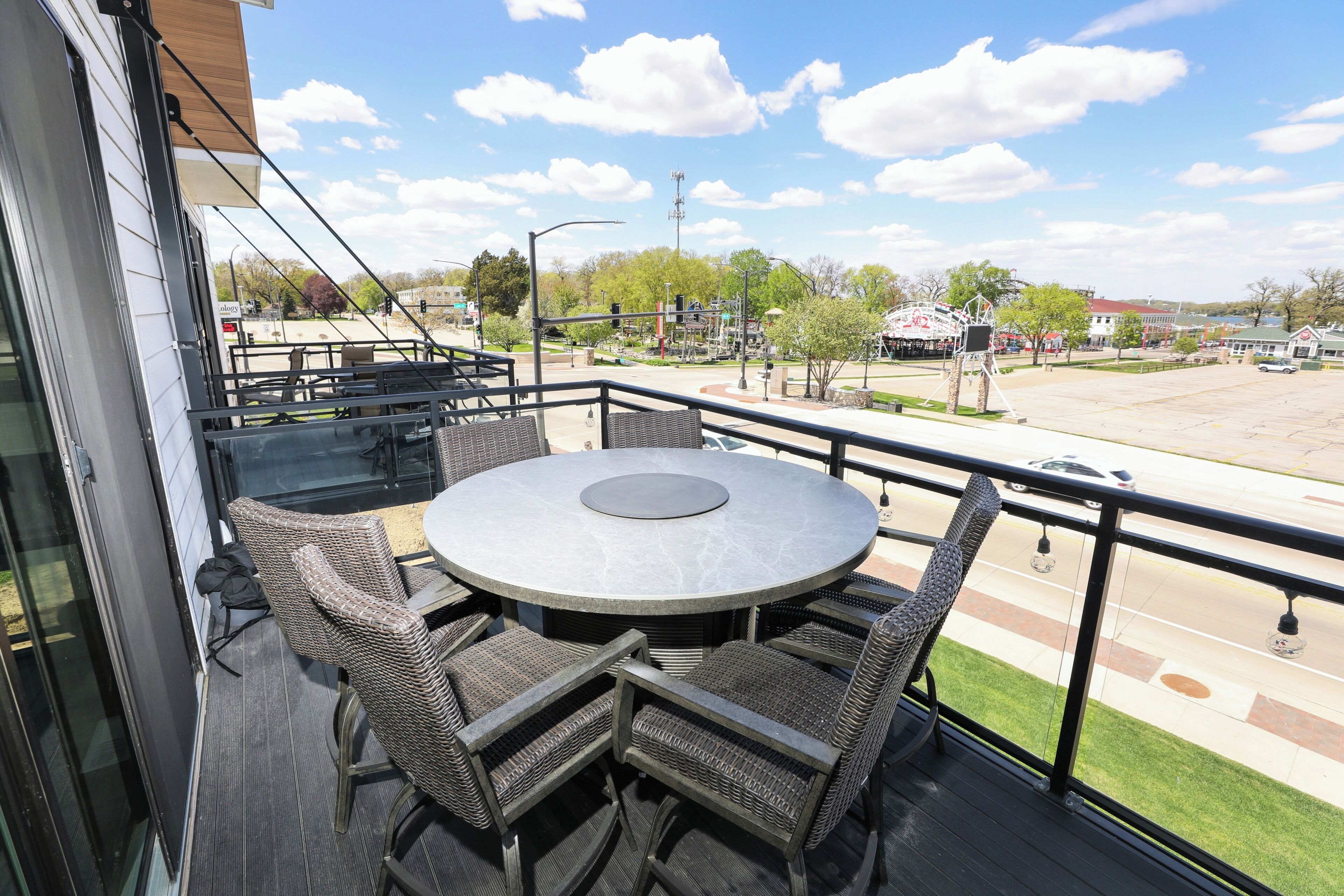 Ein Balkon mit rundem Tisch und Korbstühlen, mit Blick auf eine Straße mit Park und Gebäuden.