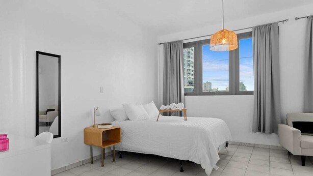A modern bedroom with a bed, bedside table, and a view of the city.