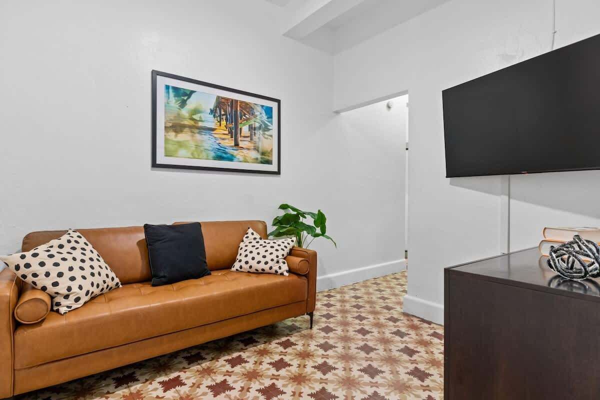 Un salon moderne avec un canapé en cuir marron, un tapis à motifs, un tableau encadré et un téléviseur à écran plat.