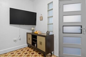 Ein Zimmer mit einem wandmontierten Flachbildfernseher, einem Holzschrank mit Schubladen, einer Tür mit satinierten Glasfeldern und einem Fußboden mit Muster.