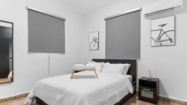Une chambre à coucher moderne avec un grand lit, une table de chevet et un climatiseur fixé au mur.
