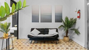 Un salon moderne avec un canapé noir, un sol à motifs et trois œuvres d’art abstraites accrochées au mur.