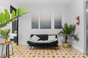 A modern living room with a black sofa, a patterned floor, and three abstract wall art pieces.