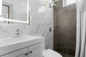 A modern bathroom with a white marble sink, a glass shower enclosure, and dark grey tiles. - Right Next To "La Placita" Apartment! Santu1A (San Juan)