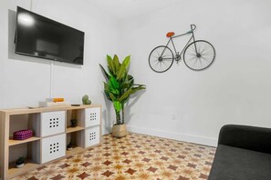 Un salon doté d’un téléviseur à écran plat, d’une bibliothèque, d’une plante en pot, d’un vélo fixé au mur et d’un sol à motifs.