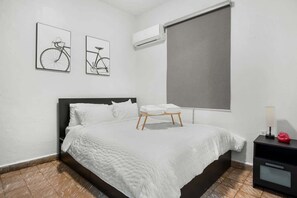 Une chambre à coucher avec un lit, une table de chevet, une fenêtre avec un store et deux vélos fixés au mur.