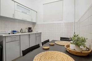 Cocina moderna con armarios blancos, encimera negra y una mesa de comedor con individuales tejidos y plantas en macetas.