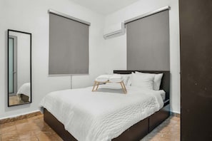 Un dormitorio con cama, un espejo y dos ventanas con persianas.