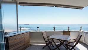 Een balkon met uitzicht op zee, een houten tafel en stoelen, en een moderne keukenhoek.