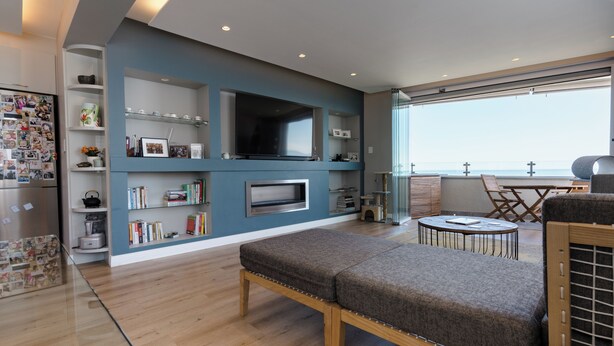 Een moderne woonkamer met een flatscreen televisie, boekenkasten, een bankje en een eethoek met uitzicht.