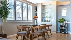 Een moderne keuken met een eethoek, met een glazen tafel en houten stoelen, een potplant en een decor kast met servies.