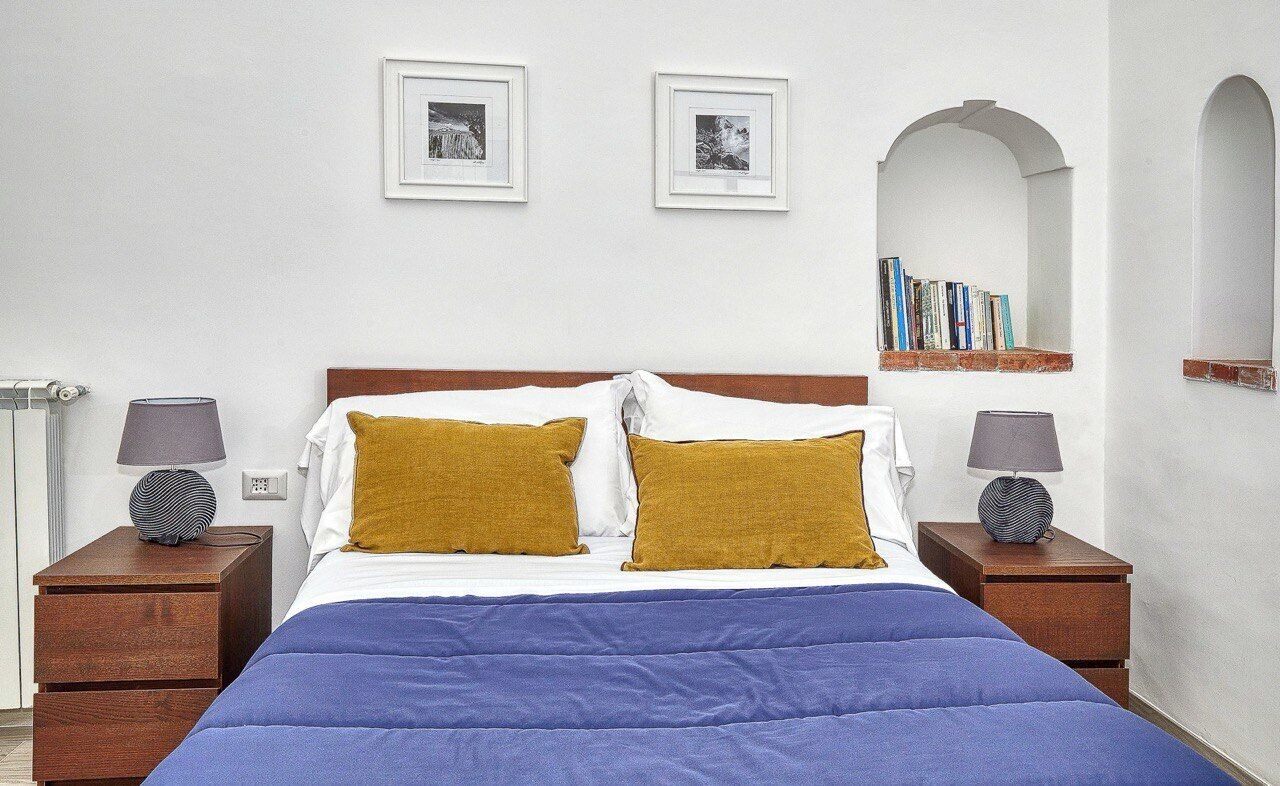 A bedroom with a bed, two nightstands, a lamp on each, a blue bedspread, and two framed pictures on the wall.