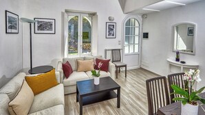 Ett modernt vardagsrum med en soffa, ett soffbord och stolar. På väggarna hänger inramade tavlor, det finns ett fönster med utsikt och en spegel.
