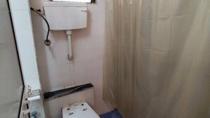 A small bathroom with a toilet, a window, and a shower curtain. - Stylish 2BHK near Lokhandwala, Kokilaben & NESCO (Mumbai)