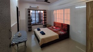 A bedroom with a bed, a table, a ceiling fan, and a window with curtains. - Stylish 2BHK near Lokhandwala, Kokilaben & NESCO (Mumbai)
