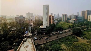 A cityscape with a prominent tall building, a busy road, and surrounding residential and commercial buildings. - Stylish 2BHK near Lokhandwala, Kokilaben & NESCO (Mumbai)