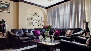 Ein Wohnzimmer mit einer schwarzen Ledersofa, einem Glastisch und einer dekorativen Vase. Eine Regalanlage mit Figuren und einem gerahmten Bild ist an der Wand angebracht.