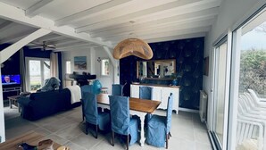 A modern living room with a dining area, large windows, and a ceiling fan. - Large villa with a marine atmosphere, 20 minutes from beaches and lakes! Ideal for families (Pontenx-les-Forges)