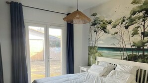 A bedroom with a large bed, a hanging light fixture, a view of the outdoors, and a painting on the wall. - Large villa with a marine atmosphere, 20 minutes from beaches and lakes! Ideal for families (Pontenx-les-Forges)