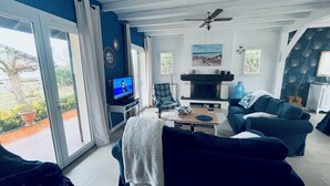 A living room with a fireplace, a television, and a view of the outdoors. - Large villa with a marine atmosphere, 20 minutes from beaches and lakes! Ideal for families (Pontenx-les-Forges)