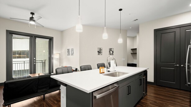 Una cocina moderna con una isla central, electrodomésticos de acero inoxidable, iluminación colgante y un ventilador de techo.