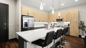 Una cocina moderna con una isla central, electrodomésticos de acero inoxidable, armarios de madera y taburetes de bar.