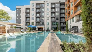 Un hotel moderno con piscina central, varios balcones y un área exterior bien cuidada con sillones y sombrillas.