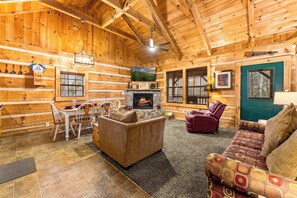 A cozy log cabin interior with a fireplace, wooden walls, a dining area, and a comfortable seating arrangement. - Cabin for 6 w Hot Tub & Game Room (Gatlinburg)
