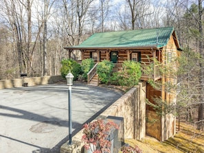 A rustic cabin with a green roof, wooden exterior, and a stone retaining wall. - Cabin for 6 w Hot Tub & Game Room (Gatlinburg)