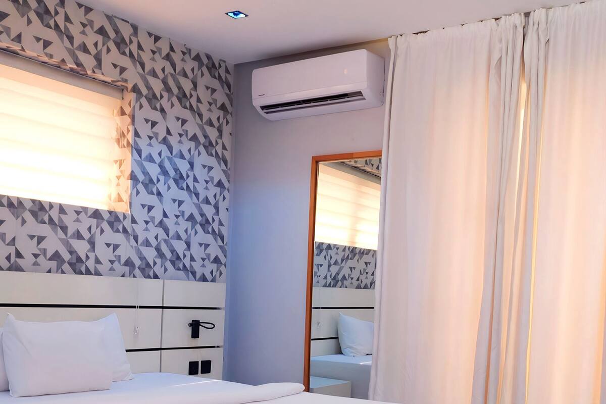 Une chambre d’hôtel moderne avec un grand lit, une table de chevet, un banc, un miroir et un papier peint à motifs.
