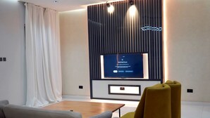 A modern living room with a flat-screen TV mounted on a wall, a sofa, a coffee table, and a yellow armchair. - 2020 Hotels katampe. (Abuja)