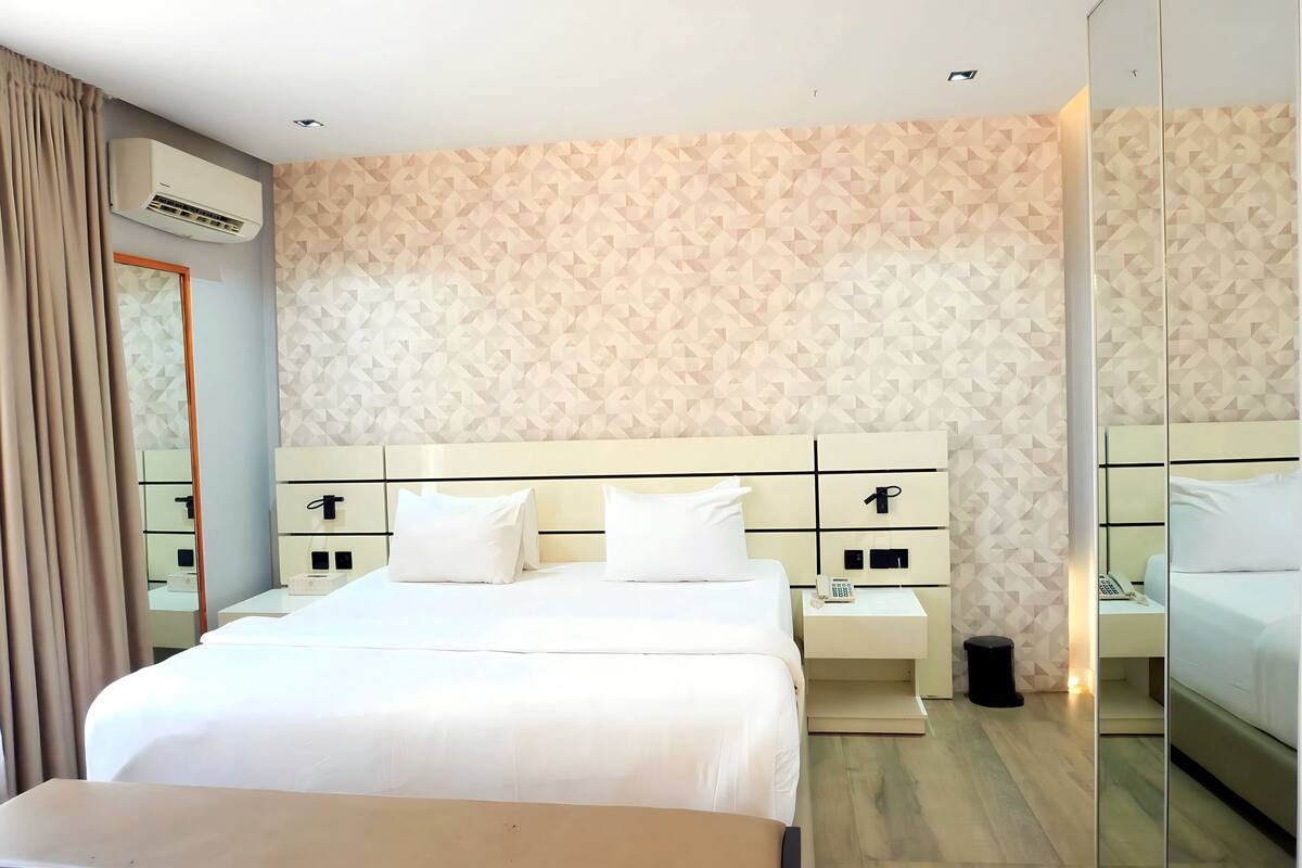 Une chambre d’hôtel avec un grand lit, des tables de chevet, un miroir et un mur orné d’un motif géométrique.