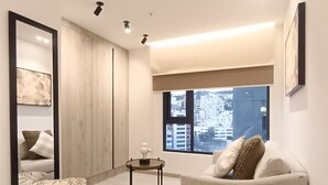 Un salon moderne avec un canapé, une table ronde, un miroir et une vue sur les immeubles par la fenêtre.