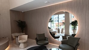 Un espace de détente moderne avec un grand miroir rond, des sièges confortables et un sol en marbre.