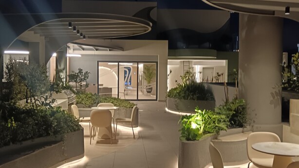 Un espace extérieur aménagé avec des chaises et des tables modernes, entouré de jardinières et d’un bâtiment au design architectural original.