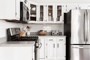 A modern kitchen with white cabinets, a stainless steel refrigerator, a microwave, a toaster, and a gas stove. - The Checkered Flag • Classic Indy Home • Walkable (Indianapolis)