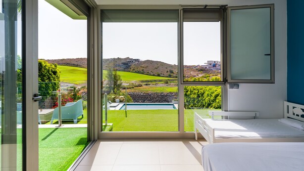 Ein Schlafzimmer mit einer großen Glasschiebetür, die auf einen Balkon mit Blick auf eine grüne Landschaft und entfernte Gebäude führt.
