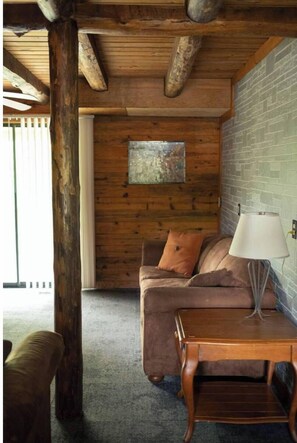 Una habitación acogedora con techo de madera, pared de ladrillo, un sofá y una mesa con lámpara.