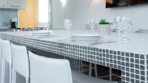 A modern kitchen with a tiled backsplash, white chairs, and a dining table set with plates, glasses, and a small plant. - Italianway Comfort - Torino 57 B (Milano)