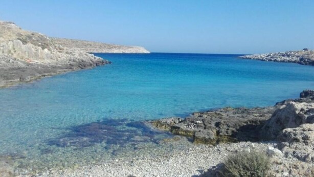 Eine Küstenlandschaft mit klarem, blauem Wasser, felsigem Gelände und einer fernen Küstenlinie.