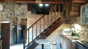 Eine rustikale Küche mit Steinwand, einer Holztreppe und einem flachbildfernseher über der Arbeitsplatte.