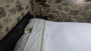 Ein Bett mit weißer Bettdecke und grünem Zierstreifen in einem Raum mit Steinwänden.