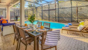 Eine sonnige Terrasse mit Pool, Esstisch, Stühlen und Liegestühlen.